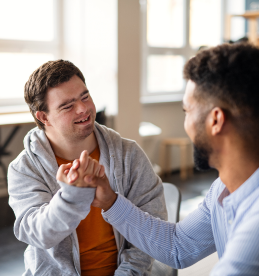 A young happy man with Down syndrome with his mentoring friend celebrating success